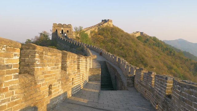 Stone stairwell leads up to the path on top of the majestic Great Wall of China. Stunning view of the ancient stone wall in rural China illuminated by the golden evening sun. Great Wall at sunrise.