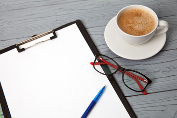 Cup of coffee, pen, glasses and an empty sheet on wooden table