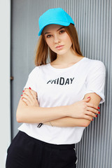 Beautiful blonde girl in a blue cap on a background of a gray wall