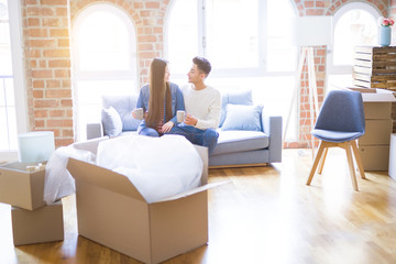 Young asian couple drinking a cup of coffee relaxing on the sofa at new home, smiling happy around cardboard boxes from moving