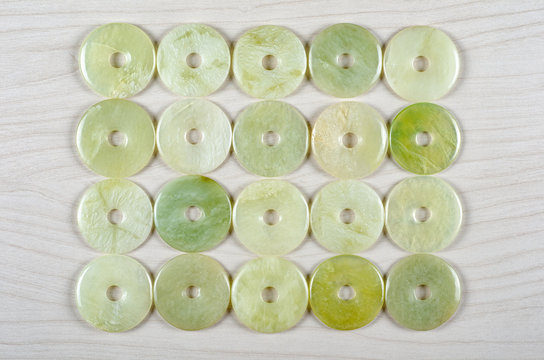Twenty butter jade round donut-shaped stones are stowed four rows. Five pieces in each one. Top view.