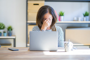 Middle age senior woman sitting at the table at home working using computer laptop tired rubbing...