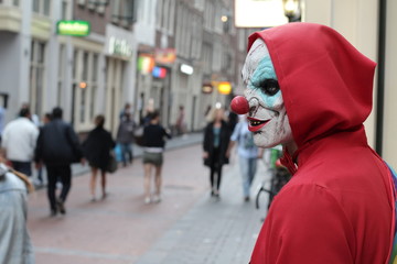 Spooky clown looking for his victim in crowded place 