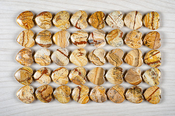 Five rows of picture jasper heart-shaped stones on white wooden background