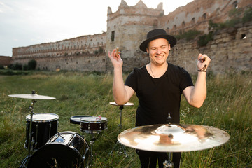 Handsome drummer emotionally plays on the drum plate, with drops water, in the countryside