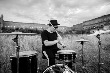 Black and white photo of musician in a black hat, plays the drums. In the open air, near ruins of the castle