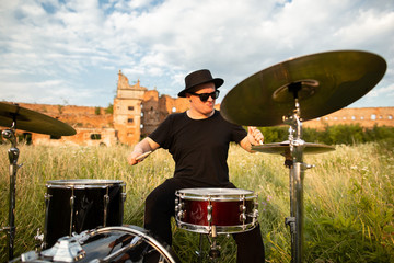 A colorful photo of musician in a black hat, plays the drums emotionally. In the open air, near...
