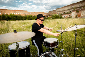 A colorful photo of musician in a black hat, plays the drums emotionally. In the open air, near...