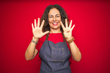 Middle age senior woman wearing apron uniform over red isolated background showing and pointing up with fingers number nine while smiling confident and happy.