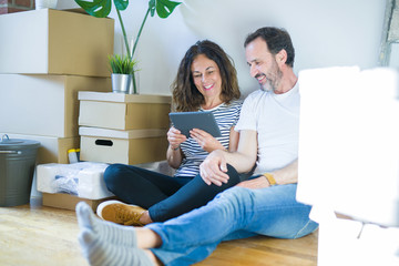Middle age senior couple moving to a new home using tablet with a happy face standing and smiling...