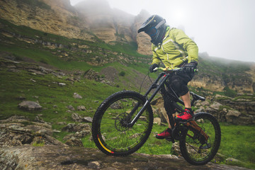 Naklejka premium Side view wide angle partly a man on a mountain bike travels on rocky terrain Against the background of cloudy sky and epic rocks. The concept of a mountain bike and mtb downhill