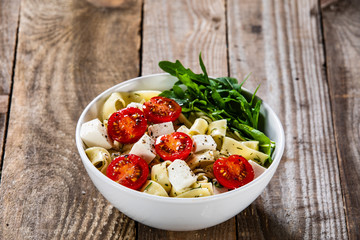 Pasta with tomatoes and white cheese on wooden table