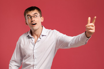 Young man in a classic white shirt is posing over a pink background.