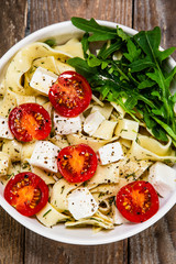 Pasta with tomatoes and white cheese on wooden table