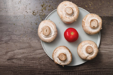 Closeup of white mushrooms with tomato on a white plate on a dark wooden table. Vegetarian healthy food