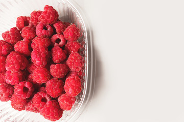 Close-up ripe juicy and delicious raspberry in a plastic transparent dish on a light background. Saturated healthy fresh food