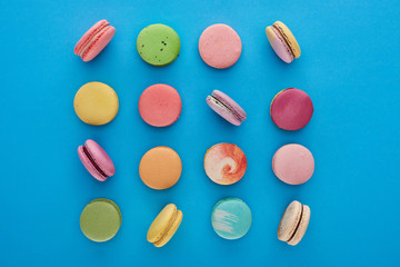 flat lay with multicolored delicious French macaroons on blue bright background