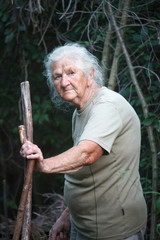 Portrait of an old woman with arthritic feet walking through the forest leaning on a stick as a...