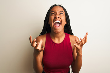 African american woman wearing red casual t-shirt standing over isolated white background crazy and mad shouting and yelling with aggressive expression and arms raised. Frustration concept.