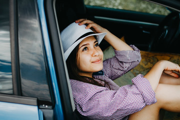 A beautiful woman is sitting in a car on a summer day in a straw hat looking up