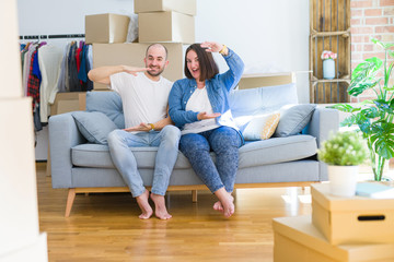 Fototapeta na wymiar Young couple sitting on the sofa arround cardboard boxes moving to a new house gesturing with hands showing big and large size sign, measure symbol. Smiling looking at the camera. Measuring concept.