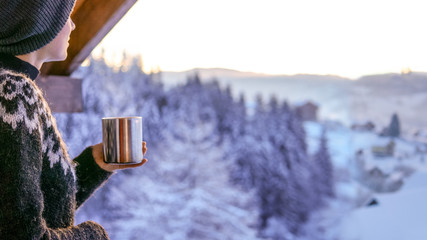 Young woman drinknig coffee with a view of the winter mountain landscape