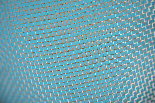 Volumetric fragment of weaving dirty metal mesh on a blue background. Rusty worn cells. Shallow depth of field