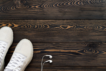 Sneakers on a dark old wooden background with headphones. Place for your text. Sport theme.