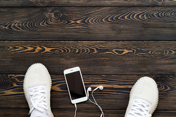 Sneakers on a dark old wooden background with a mobile phone and headphones. Place for your text.
