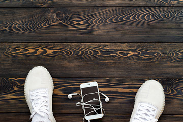 Sneakers on a dark old wooden background with a mobile phone and headphones. Place for your text.