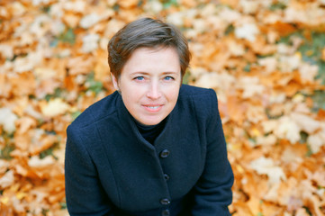 Beautiful woman posing with yellow leaves in autumn city park, fall season