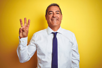 Handsome middle age businessman standing over isolated yellow background showing and pointing up with fingers number three while smiling confident and happy.