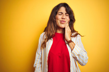 Young beautiful woman wearing red t-shirt and stripes shirt over yellow isolated background touching mouth with hand with painful expression because of toothache or dental illness on teeth. 