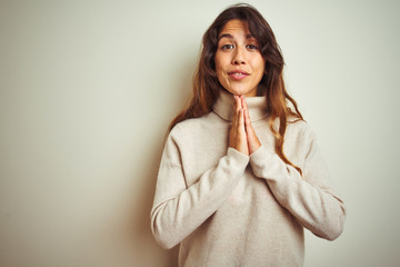 Young beautiful woman wearing winter sweater standing over white isolated background praying with hands together asking for forgiveness smiling confident.