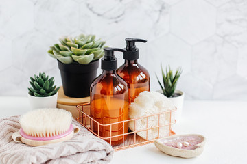 Soap and shampoo bottles and cotton towels with green plant on white table inside a bathroom background.