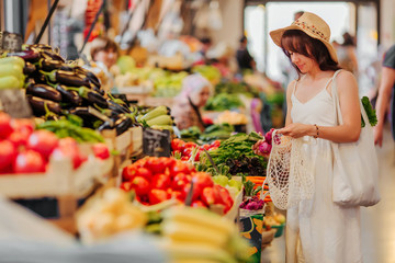 Young Woman puts fruits and vegetables in cotton produce bag at food market. Reusable eco bag for...