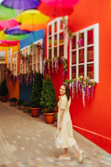 Obraz premium Travel tourist brunette woman in yellow dress walks the streets with bright decoration of the city. Tilt-shift lens blur