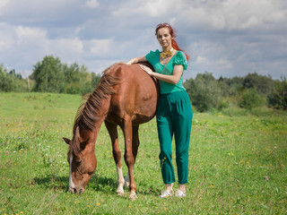 Young attractive caucasian girl on a summer pasture embraces the grown-up red foal