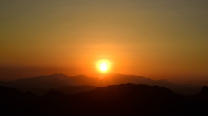 sun setting behind a dense forest area followed by mountains.