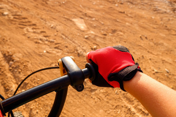 Fist of a boy with red cyclist gloves pedaling on a dirt track.