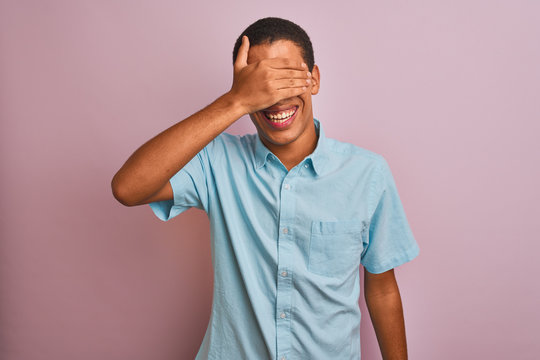 Young handsome arab man wearing blue shirt standing over isolated pink background smiling and laughing with hand on face covering eyes for surprise. Blind concept.