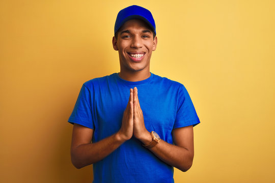 Young handsome arab delivery man standing over isolated yellow background praying with hands together asking for forgiveness smiling confident.