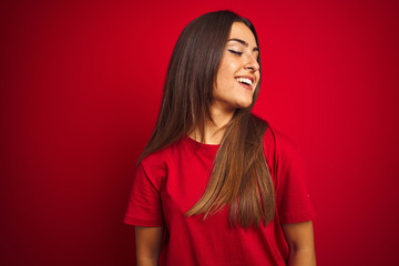 Young beautiful woman wearing t-shirt standing over isolated red background looking away to side with smile on face, natural expression. Laughing confident.