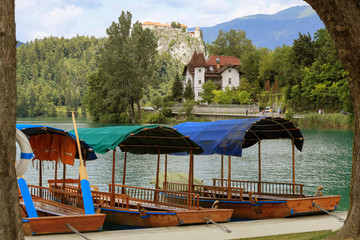 Lake Bled with traditional boats. Beautiful mountain lake in summer with small Church on island with castle on cliff and alps in the background.