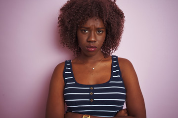 Young african afro woman wearing striped t-shirt standing over isolated pink background skeptic and...