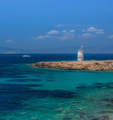 The wild coast of Aegina island with clear and blue waters of Mediterranean sea and the old small lighthouse in the background, in Saronic gulf, Greece.