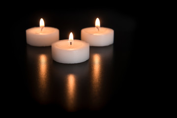 Three burning tea lights with their reflection on a black background