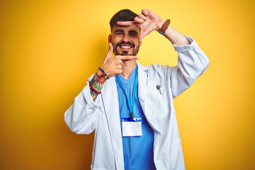 Young doctor man with tattoo wearing id card standing over isolated yellow background smiling...