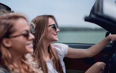 two fashionable girls travel in a convertible car.