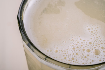 Fresh cold drink beverage frothy kvass in faceted glass on white wooden background, close up